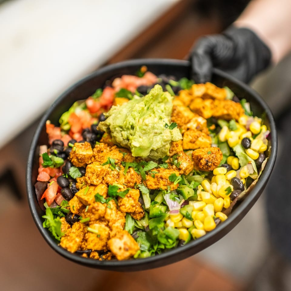 A black bowl of Amaya's Fresh Mexican Grill burrito bowl with chicken, guacamole, corn, and beans.