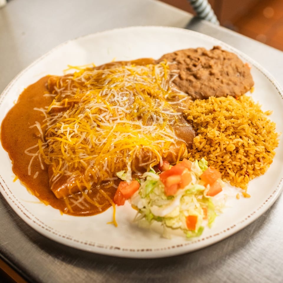 Amaya's enchiladas covered in red sauce and cheese, with a side of rice, beans, and salad.