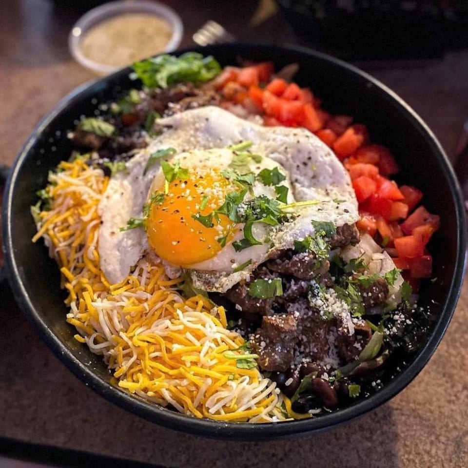 Mexican breakfast bowl with steak, black beans, cheese, diced tomatoes, and a fried egg.