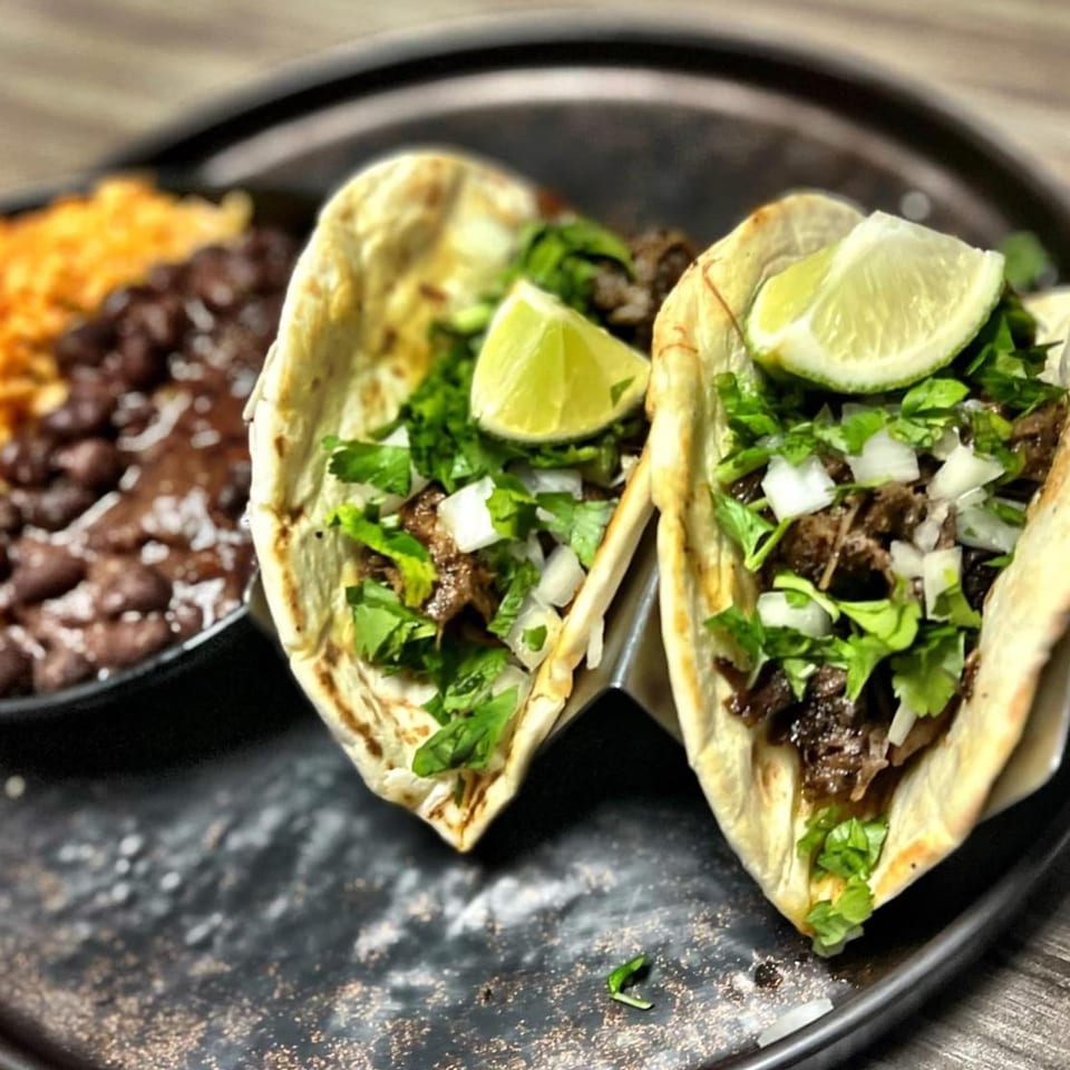 Two carne asada tacos with cilantro, onions, and lime, alongside rice and beans.