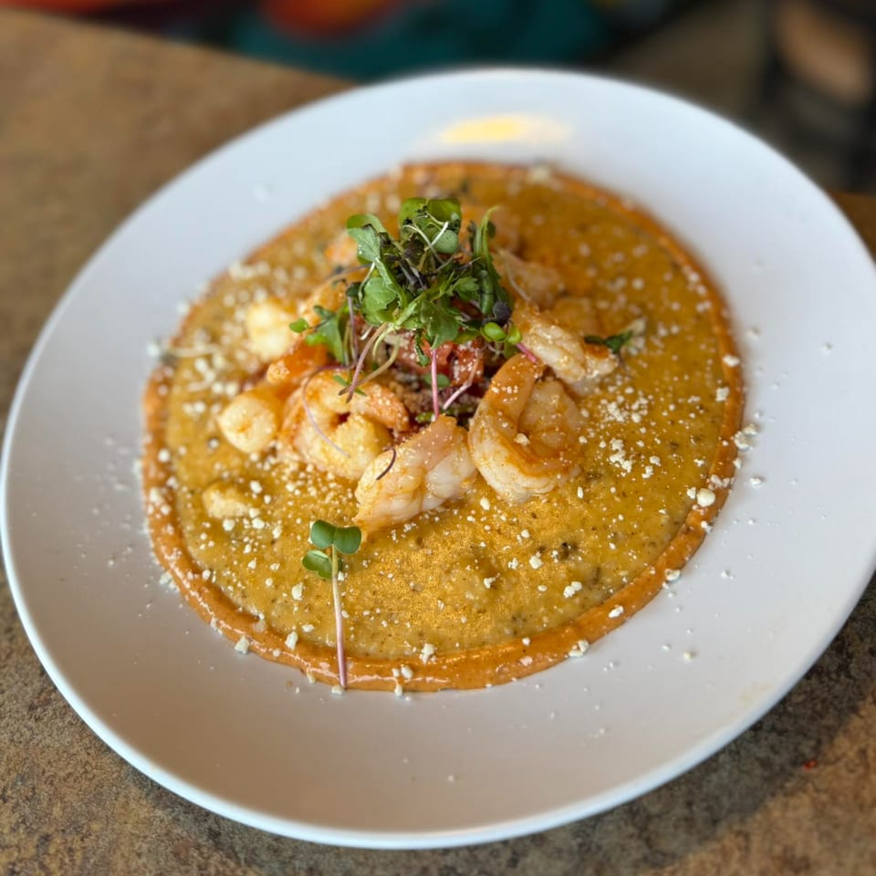 Amaya's Fresh Mexican Grill's shrimp and grits, garnished with microgreens and cheese on a white plate.