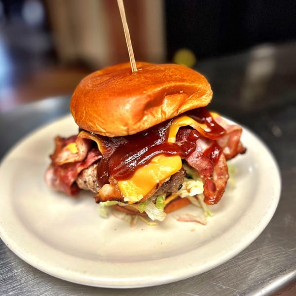 A juicy burger with melted cheese, crispy bacon, and BBQ sauce on a white plate.
