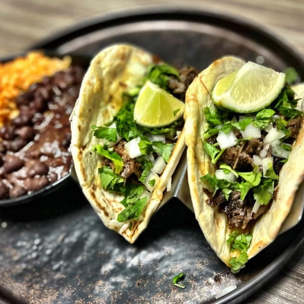 Two Amaya's Fresh Mexican Grill tacos with meat, cilantro, onions, and lime, served with rice and beans.