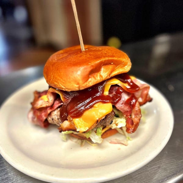 A juicy burger with bacon, melted cheese, and BBQ sauce on a white plate.