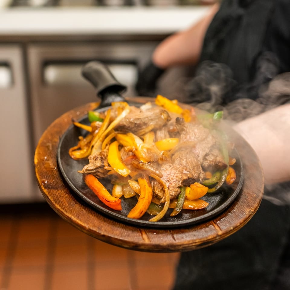 Steaming Amaya's Fresh Mexican Grill fajitas with beef, onions, and bell peppers on a sizzling platter.