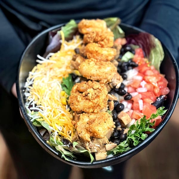 A vibrant Mexican shrimp bowl with lettuce, cheese, black beans, tomatoes, and fried shrimp.