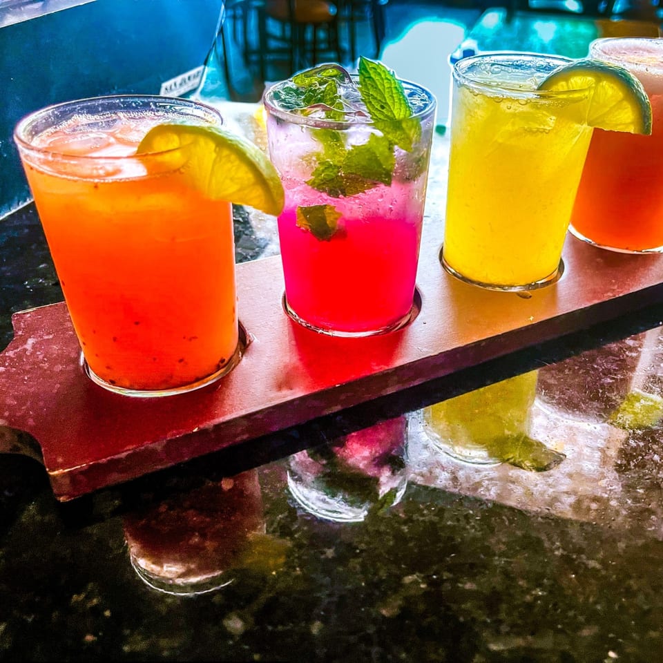 Four vibrant Mexican drinks, including margaritas and mojitos, on a wooden serving board.